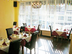 Legends Hotel dining room showing tables on the left and right with pink cloths and glass table tops. Legends Hotel front window is featured.